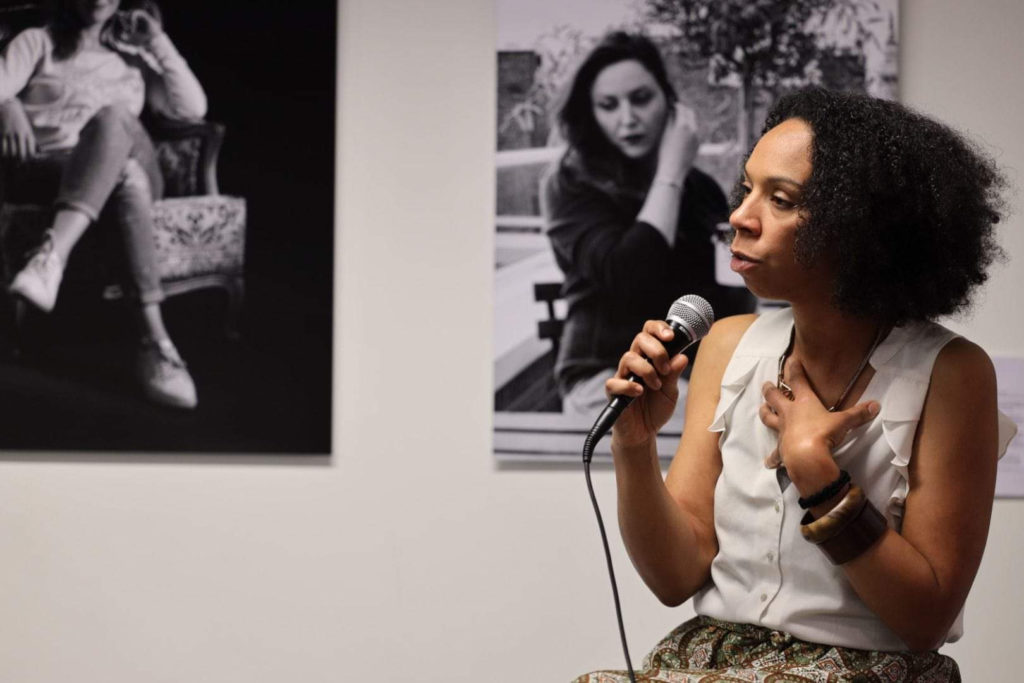 photo de Nafi Yao micro à la main lors de présentation du livre au Centre Culturel de Herstal en Belgique. En arrière plan, une photo de Julie Foulon, Girleek.