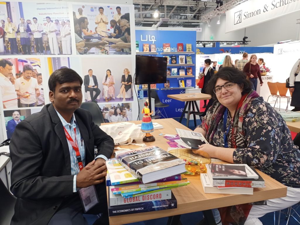 Joselin Jaba, membre de l’équipe du Fellowship de Chennai en Inde, et Cindy Vandermeulen, assis·es à une table lors d’un salon international du livre, entouré·es d’ouvrages.
