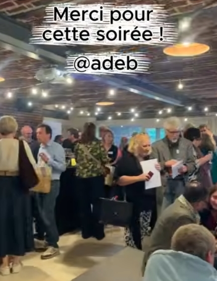 capture d'écran d'une vidéo prise lors de l'assemblée générale de l'adeb on l'on voit plusieurs personnes discuter et porter des toasts.